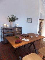 Ein Tisch, auf dem eine Rose, Stein, Windlicht, Herz und Bücher liegen. Im Hintergrund stehen Kerzen auf einem Schrank.